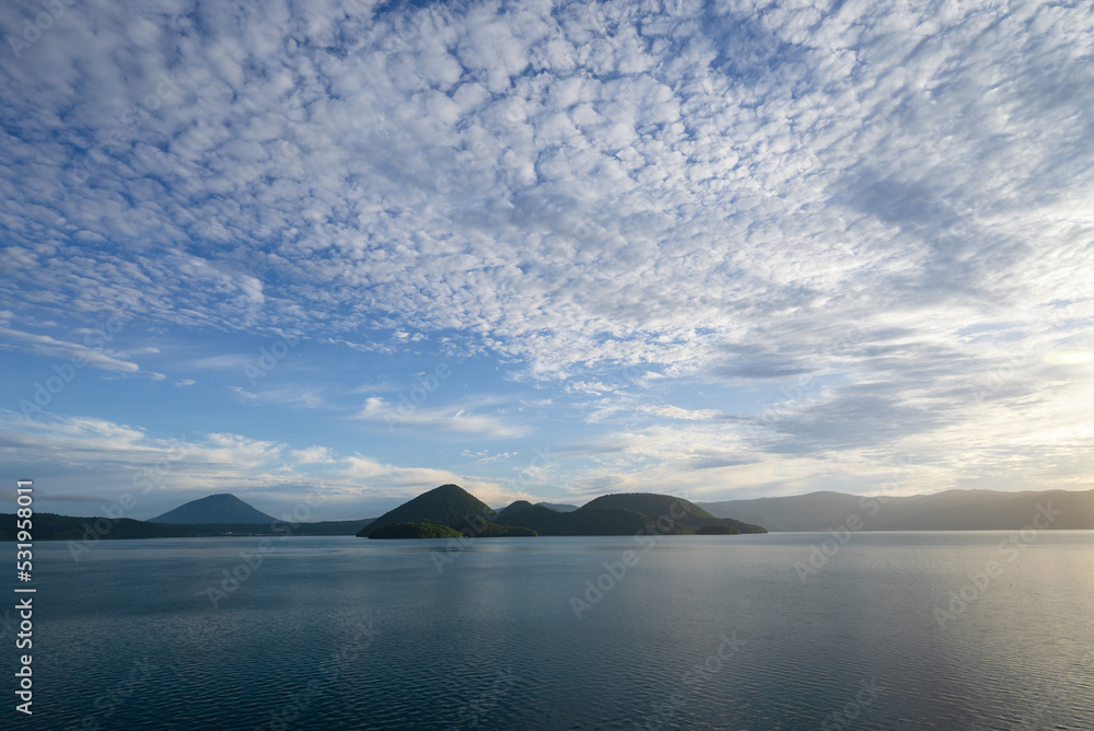 青空と流れゆく白い雲と朝日を映す洞爺湖面