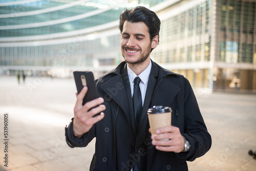 Handsome elegant dressed man using his smartphone and holding a cup of coffee