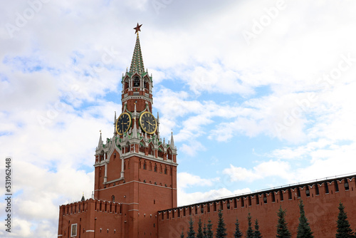 Red square in Moscow with Kremlin tower, chimes and brick wall on background of blue sky with clouds. Symbol of Russian authorities