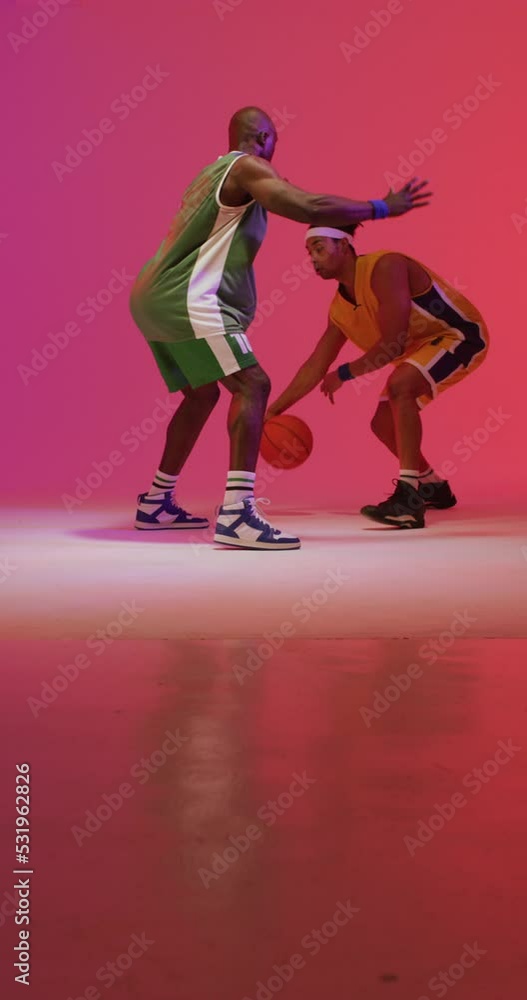 Vertical video of two diverse male basketball players playing with ball on pink background Vertical video of two diverse male basketball players playing with ball on pink background