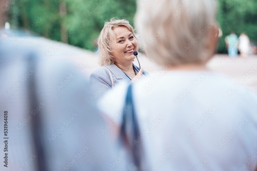 female tour guide with a microphone standing among a group of tourists.