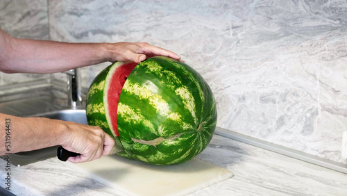 A man cuts a large watermelon with a knife. senior man cutting a ripe juicy red watermelon in half on cutting board. Close up shot of men's hands holding watermelon. summer fruit concept