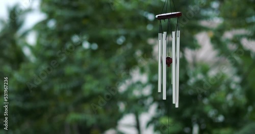 Wind Chimes hangs on the porch of the house against the backdrop of green trees photo