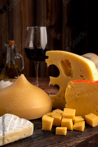 Varied cheese table, blue cheese Fontina Gruyer Cheese Teetilla in wooden table with red wine glass Pimentero oil and Round homemade fields of field and rustic knife photo