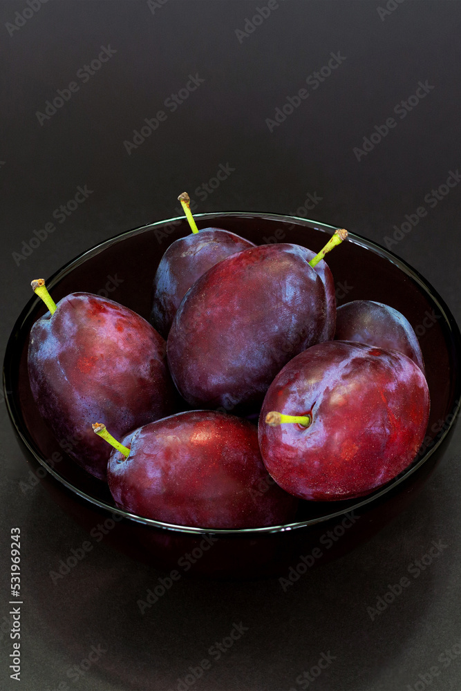 Fresh plum. Autumn harvest. Ripe purple plums in glass bowl on dark background. Concept: seasonal fruits, healthy food. Top view. Close up. Vertical. Copy space