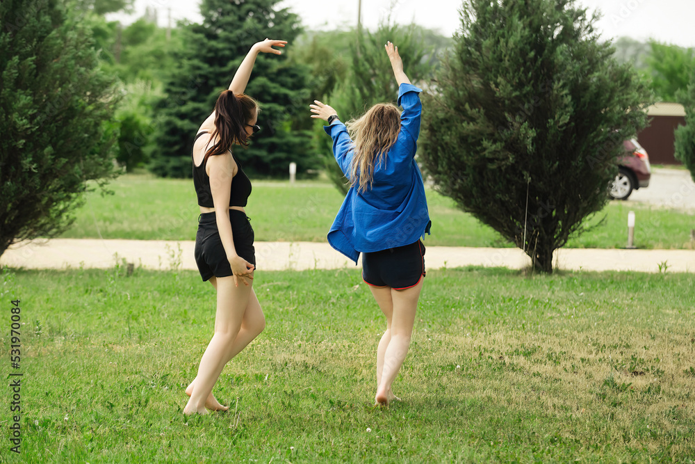 Obraz premium two beautiful girls girlfriends have fun and dance in the summer on vacation, dressed in swimwear and sportswear on a bright green meadow
