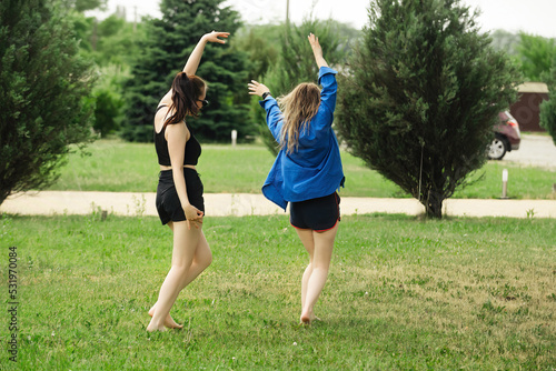 two beautiful girls girlfriends have fun and dance in the summer on vacation, dressed in swimwear and sportswear on a bright green meadow