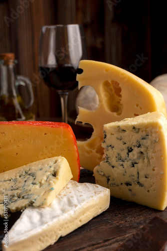 Varied cheese table, blue cheese Fontina Gruyer Cheese Teetilla in wooden table with red wine glass Pimentero oil and Round homemade fields of field and rustic knife photo