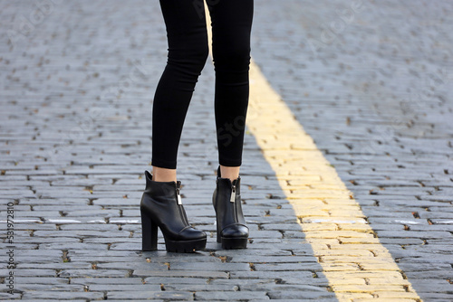 Female legs in black jeans and boots on high heels. Slim girl standing on a street, fashion in autumn city