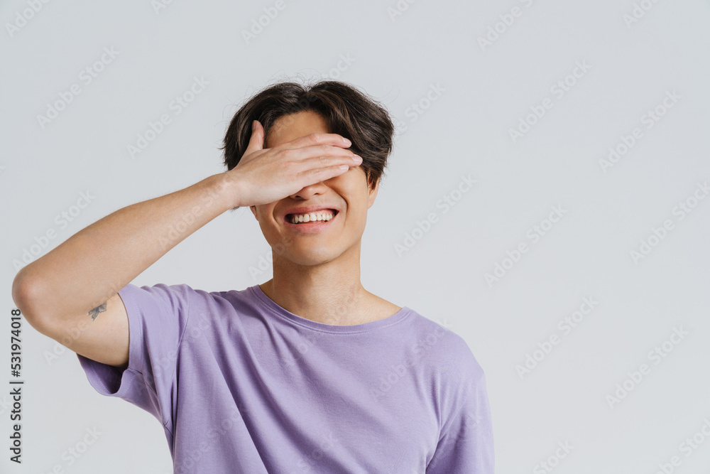 Young asian man wearing t-shirt smiling and covering his eyes Young asian man wearing t-shirt smiling and covering his eyes
