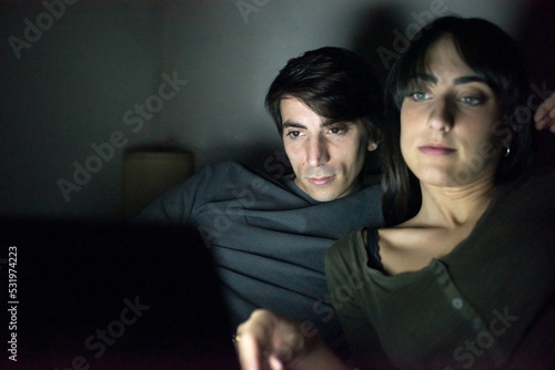 Young couple using laptop computer on bed at night time