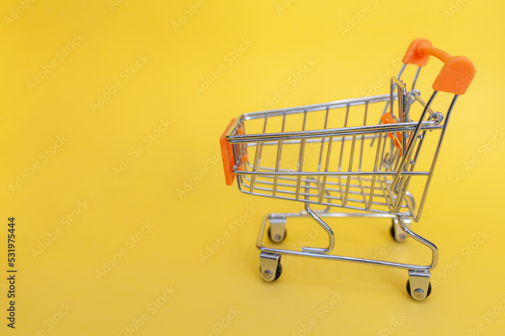 Small supermarket grocery push cart for shopping. Shopaholic. Buyer. Shopping concept. Close-up. Isolated shopping trolley on a yellow background. Copy space. Small supermarket grocery push cart for shopping. Shopaholic. Buyer. Shopping concept. Close-up. Isolated shopping trolley on a yellow background. Copy space.