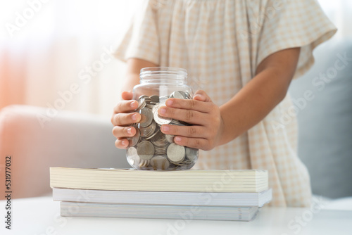 Little girl save money coins for education in piggy bank on the book stack