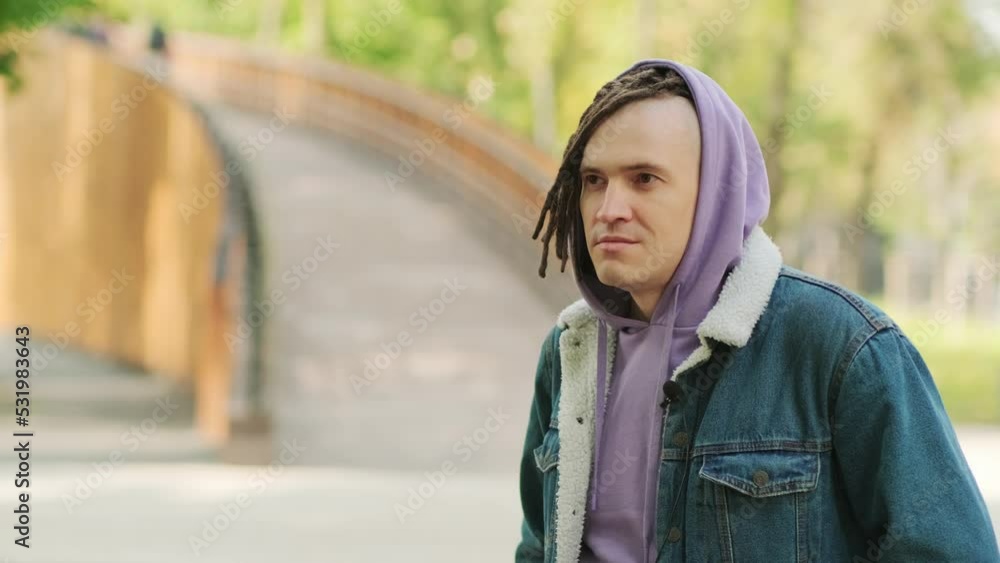 Portrait of handsome man with brown dreadlocks in hoodie, denim jacket posing on street in city park. Portrait of handsome man with brown dreadlocks in hoodie, denim jacket posing on street in city park.