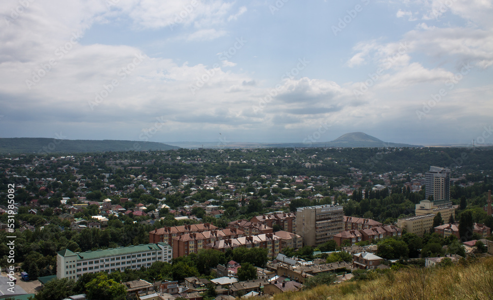 Panoramic top view of Pyatigorsk, Stavropol territory with residential buildings among green trees and cloudy sky above the horizon
