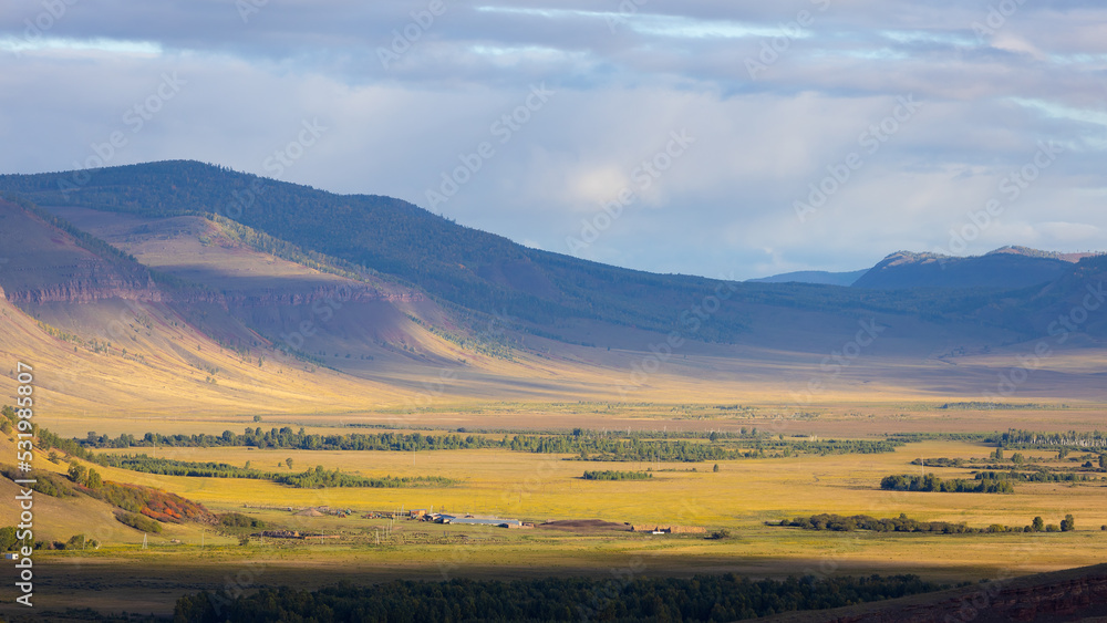 Autumn landscape with mountain valley in the haze at sunny evening. Mountain range Sunduki in Khakassia, Russia. Shadow of the clouds lies on the slopes of the mountains. Top view