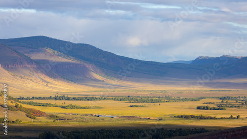 Autumn landscape with mountain valley in the haze at sunny evening. Mountain range Sunduki in Khakassia, Russia. Shadow of the clouds lies on the slopes of the mountains. Top view photo