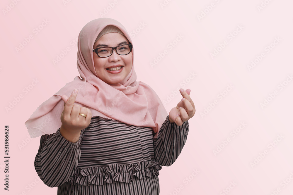 Portrait of cheerful Asian woman with hijab, showing finger sign of Korean love. Isolated image on pink background Portrait of cheerful Asian woman with hijab, showing finger sign of Korean love. Isolated image on pink background