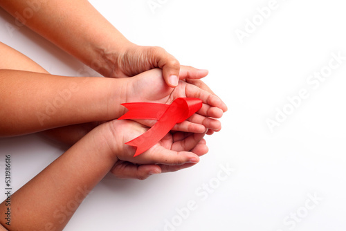 Woman's hand and child's hand holding red ribbon together over white with copyspace. Aids day concept photo