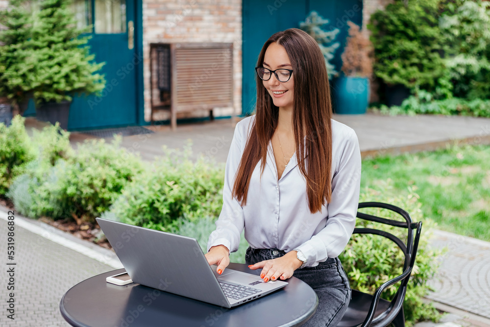 A young woman in glasses sits at a table in a cafe and works at a laptop A young woman in glasses sits at a table in a cafe and works at a laptop