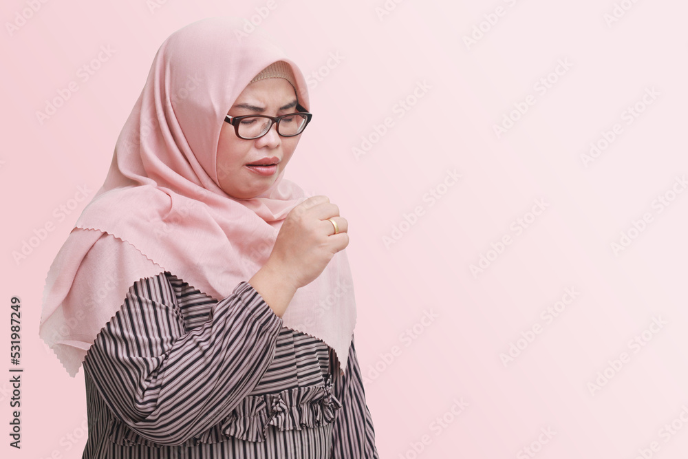 Portrait of unpleasant Asian woman with hijab keeping hand palm covering her mouth while coughing with closed eyes. Isolated image on pink background Portrait of unpleasant Asian woman with hijab keeping hand palm covering her mouth while coughing with closed eyes. Isolated image on pink background