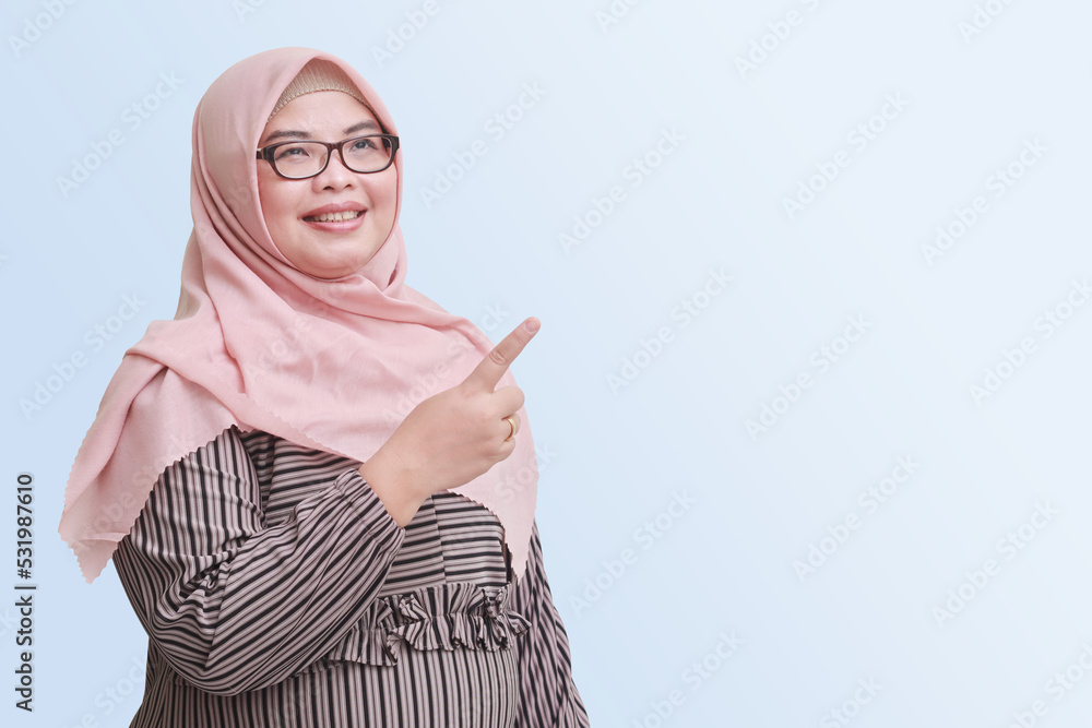 Portrait of cheerful Asian woman with hijab, showing product, pointing ...