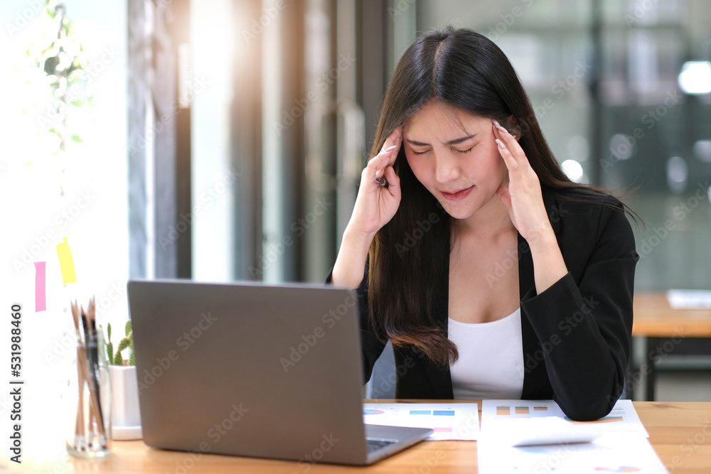 Young Asian woman feeling migraine head strain. Tired, Overworked businesswoman financier while working on laptop computer in office. Young Asian woman feeling migraine head strain. Tired, Overworked businesswoman financier while working on laptop computer in office.
