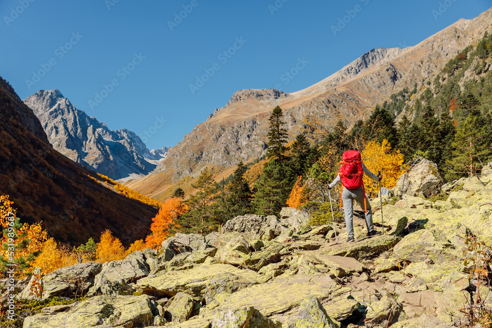 Traveller woman with red backpack walking in the autumnal mountains. Mountain and tourist