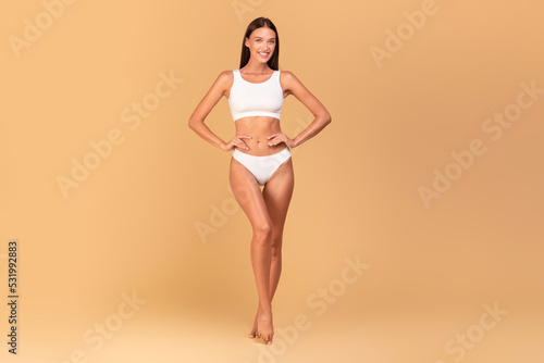 Cuadro en lienzo Sensual young woman posing in white underwear over beige studio background, show