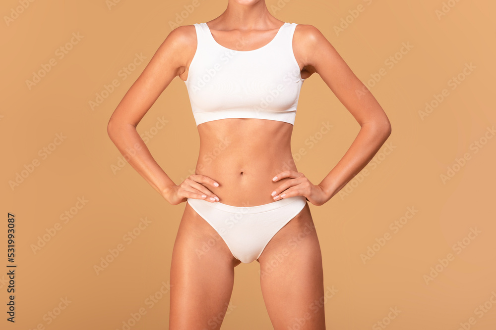 Young slender lady posing in white underwear over beige studio background, showing her beautiful curves, cropped