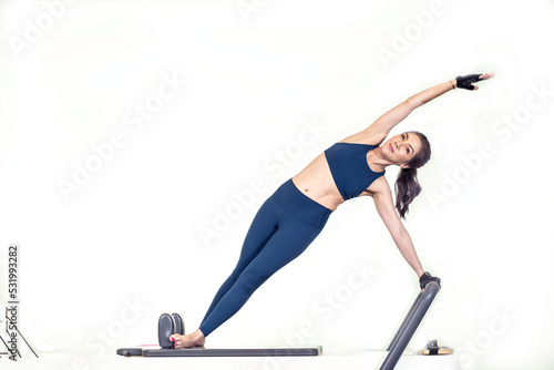 Fototapeta Naklejka Na Ścianę i Meble -  The instructor does exercises on the reformer, a beautiful girl trains on the modern reformer simulator to work out deep muscles, the modernized reformer equipment for Pilates and yoga.