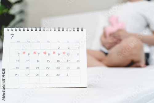 Monthly menstruation symptom period concept. Close up calendar marking on menstruation period day and woman have stomach pain as background. photo