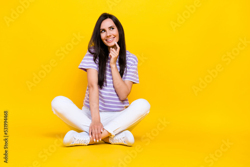 Photo of pretty sweet minded lady sit floor arm touch face interested look empty space cunning creative plan isolated on yellow background