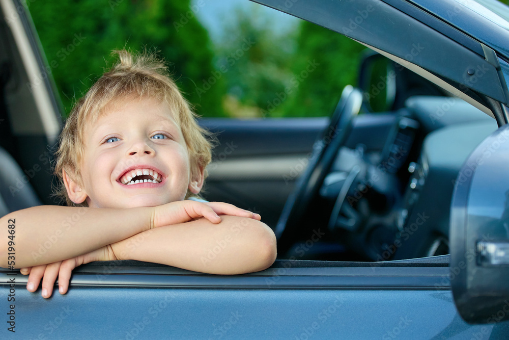 Funny boy folded his hands on the open car window, smiling broadly with joy. Happy Child in the passenger seat waiting for a long-awaited trip Funny boy folded his hands on the open car window, smiling broadly with joy. Happy Child in the passenger seat waiting for a long-awaited trip