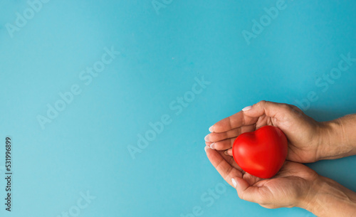 Women's hands hold a small red heart on a blue background, on the left is a copyspace.The concept of a thrifty attitude to the heart, woman's health. Give care. mother's day, loving female heart