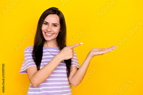 Photo of young attractive gorgeous nice woman hold hand finger pointing new product recommend isolated on yellow color background