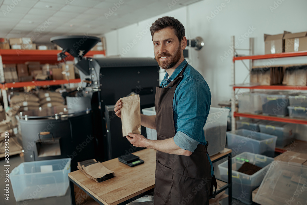 Business owner holding roasted coffee beans in paper bag in coffee factory Business owner holding roasted coffee beans in paper bag in coffee factory