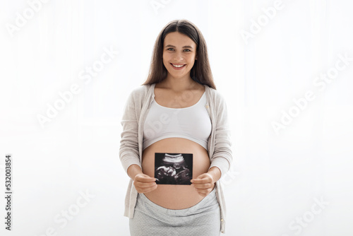 Happy pregnant woman holding ultrasound image, white background