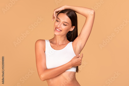 Reducing body odor. Happy fit lady standing with one hand up, demonstrating her smooth depilated armpit photo