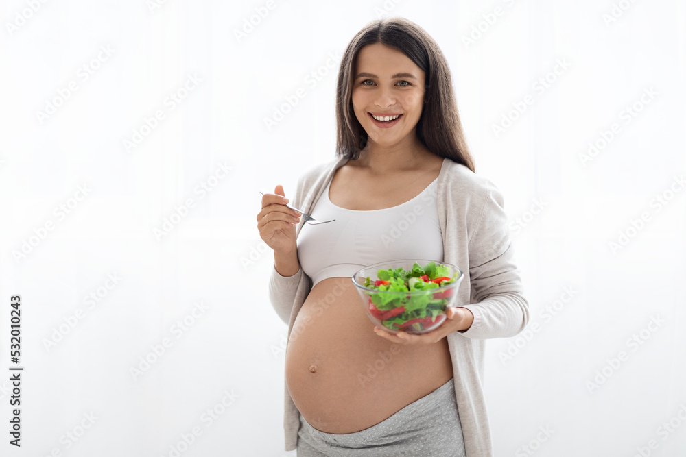 Happy pregnant woman holding bowl with fresh salad and fork Happy pregnant woman holding bowl with fresh salad and fork