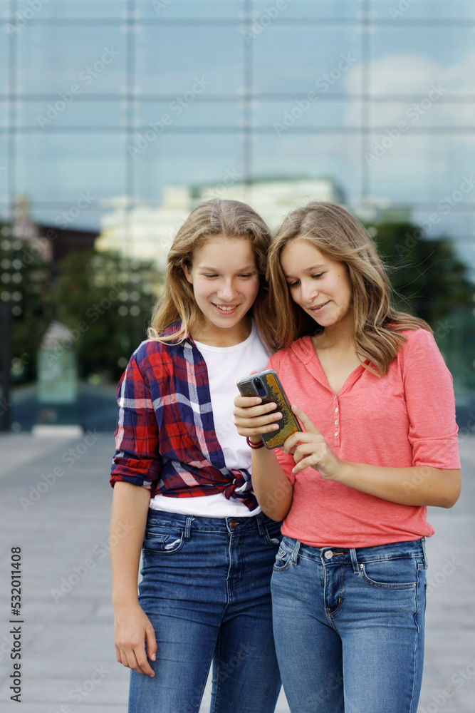 Two teenage girlfriends playing with a smartphone, checking social medias