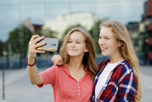 Two teenage girlfriends taking selfie, playing with a smartphone, using social medias