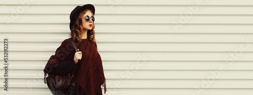 Portrait of stylish woman model posing wearing black round hat and knitted brown poncho on white background © rohappy