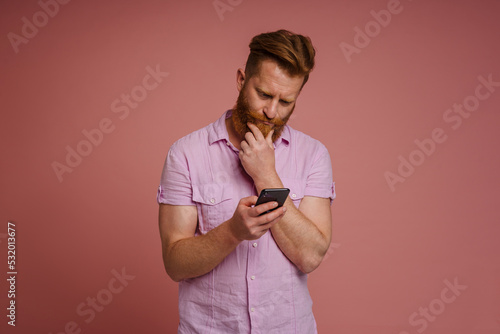 Canvas Print Ginger white man with beard frowning and using mobile phone