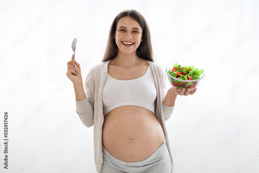 Good-looking pregnant lady holding bowl with salad and fork