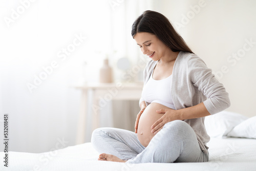 Smiling pregnant woman sitting on bed in her bedroom