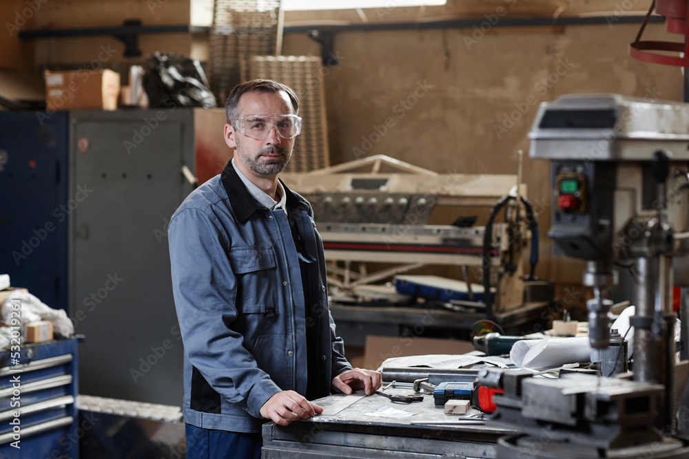Waist up portrait of mature worker looking at camera while standing in factory workshop, copy space Waist up portrait of mature worker looking at camera while standing in factory workshop, copy space