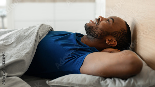 Happy Black Man Lying Holding Hands Behind Head In Bedroom