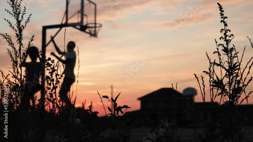 4k video Silhouettes of basketball players at the beautiful sunset. Amazing cinematic sport shoot. Two male playing street ball outside.