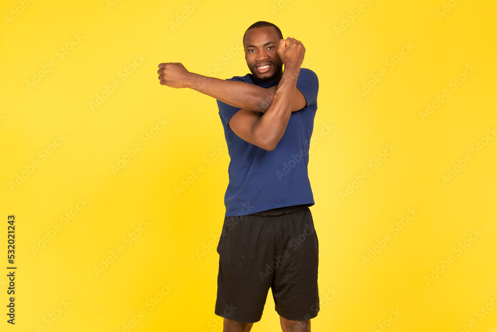 African Man Exercising Stretching Arms Having Fitness Workout, Yellow Background